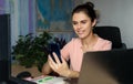 Smiling young woman working home near laptop, holds phone, press button and looks to screen. World map in the background Royalty Free Stock Photo