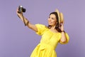 Smiling young woman in yellow dress, summer hat doing selfie on retro vintage photo camera isolated on pastel violet Royalty Free Stock Photo