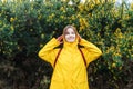 Smiling young woman in a yellow raincoat and hood enjoying walk on background of blooming bush with flowers. Travel Royalty Free Stock Photo