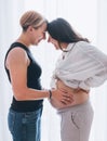 Smiling young women couple next to living room window. Tender touching partner's pregnant belly. health, happy pregnancy