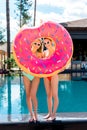 smiling young women looking at camera through inflatable ring in shape of bitten donut