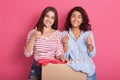 Smiling young women posing near box full of clothes, showing thumb up recommend donating apparel to needy people, happy females