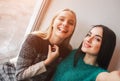 Smiling young women taking selfie while drinking coffee indoors at lunch meeting. Royalty Free Stock Photo