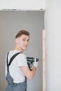 Smiling young working man in overalls drills screws with an electric screwdriver in an apartment