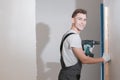 Smiling young working man in overalls drills screws with an electric screwdriver in an apartment