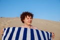 Smiling young 32 years old Caucasian man with curly hair with striped towel on sandy beach on sand dune. Closeup summer headshot Royalty Free Stock Photo