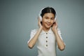 Smiling youthful Asian girl touching headphones while listening to music