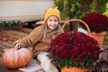 Smilling Child in autumn garden with yellow pumpkins and flower. Happy little girl sitting on porch of house with chrysanthemums p Royalty Free Stock Photo