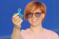 Smilling girl in pink t-shirt is playing blue metal spinner in hands on the street, woman playing with a popular fidget spinner to