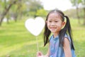 Smilling little Asian girl holding blank heart label lying on green grass at summer garden