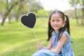 Smilling little Asian girl holding blank heart label lying on green grass at summer garden Royalty Free Stock Photo