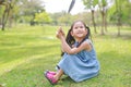 Smilling little Asian girl holding blank heart label lying on green grass at summer garden