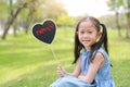 Smilling little Asian girl holding heart label with text `FAMILY` lying on green grass at summer garden