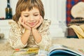 Smilling little Caucasian girl lying on the floor and reading an illustrated book.