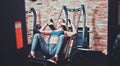 Smilling sportswoman doing squatting in training machine.