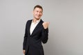 Smirked young business man in classic black suit, shirt pointing thumb aside behind his back isolated on grey wall Royalty Free Stock Photo