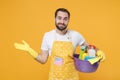 Smirked young man househusband in apron rubber gloves hold basin with detergent bottles washing cleansers doing Royalty Free Stock Photo