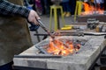 The smith heats a metal detail in a forge brazier