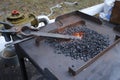 Blacksmith hand holds forceps with a metal billet in a burning forge glowing it red. At the smithy workshop