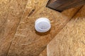 Smoke and carbon monoxide detector with a central LED, mounted on a ceiling lined with OSB boards.