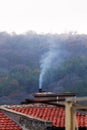 Smoke from the chimney of a house on the roof against the background of a foggy forest Royalty Free Stock Photo