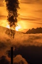 Smoke from chimny and colorful sky with sun and mountains at background