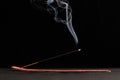 Smoke curls of burning incense stick in wooden holder for relaxation and meditation black background