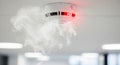 Smoke detector on ceiling warning about potential fire with red light blinking and white smoke. Safety device for home and office Royalty Free Stock Photo