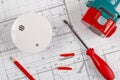 Smoke detector or fire alarm sensor on white architectural plans background with drill, screwdriver and screws, house safety or Royalty Free Stock Photo