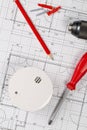 Smoke detector or fire alarm sensor on white architectural plans background with drill, screwdriver and screws, house safety or Royalty Free Stock Photo