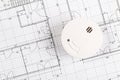 Smoke detector or fire alarm sensor on white architectural plans background, house safety or security concept, copy space, top Royalty Free Stock Photo