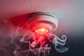 Smoke detector with glowing red light in white smoke, indicating alarm or malfunction