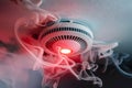 Smoke detector with glowing red light in white smoke, indicating alarm or malfunction