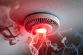 Smoke detector with glowing red light in white smoke, indicating alarm or malfunction