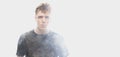 Smoke enveloped young man. Model looking at camera  over white background with clouds of smoke. Concept of Royalty Free Stock Photo