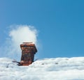 Smoke out of a brick chimney on a snowy rooftop home