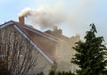 Roof with smoking chimney and trees in autumn