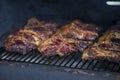 Smoke rising around a slow cooked beef brisket on the grill grates of a smoker barbecue. Grilled spare ribs macro - pork ribs Royalty Free Stock Photo