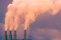 Smoke and steam rising into the air from power plant stacks; dark clouds background; concept for environmental pollution and