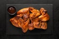 Smoked chicken wings on a slate board and barbecue sauce in a bowl on a rustic black background