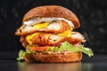 Smoked chickenburger centred on black backgrounds with double schnitzel, onion, cheddar, iceberg lettuce, tomato and