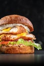 Smoked chickenburger centred on black backgrounds with double schnitzel, onion, cheddar, iceberg lettuce, tomato and