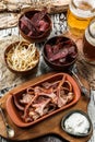 Smoked cured pork's ears, bacon, lard, dried squid, Sujuk, Basturma in bowl and two glasses of beer in wooden background