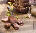 Smoked dried gammon ham and slices of sausages with bread, tomatos, herbs, garlic and basketson wooden board Royalty Free Stock Photo