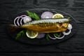 Smoked fish mackerel with onion and lemon on a black plate. Top view. Free space for your text. Royalty Free Stock Photo