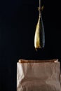 Smoked fish mackerel on the paper bag in the black wooden background