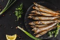 Smoked fishes sprat marinated with spices, salt, greens and slice of bread on plate over dark stone background. Mediterranean food
