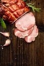 Smoked gammon sliced on a wooden rustic table with addition of fresh aromatic herbs.