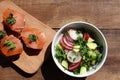 Smoked salmon canapes on rye bread with cream cheese and parsley on cut board and fresh vegetable salad in white bowl Royalty Free Stock Photo