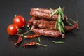 Smoked sausage with rosemary, pepper, tomatoes and garlic on a black background. Royalty Free Stock Photo
